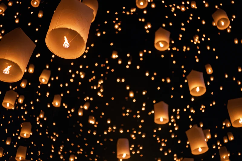 Paper sky lanterns floating upward into the night sky during a festival celebration