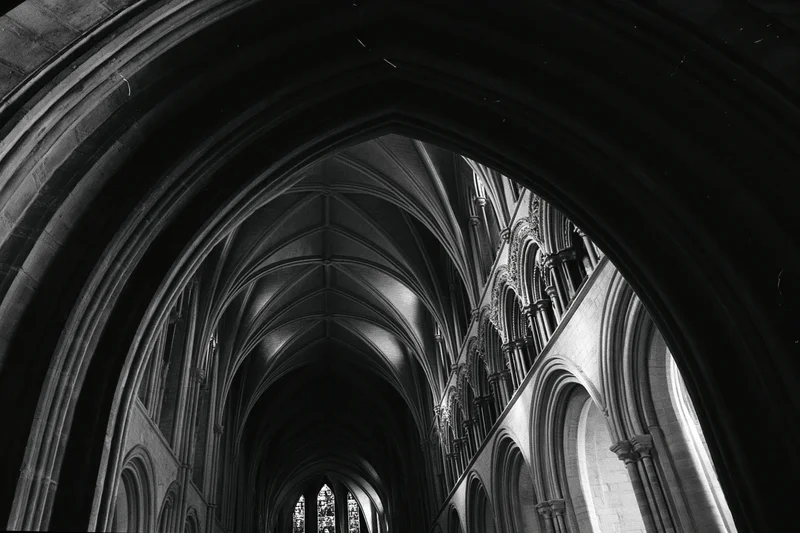 Gothic cathedral nave interior viewed through sweeping stone arches with ribbed vaults and stained glass windows