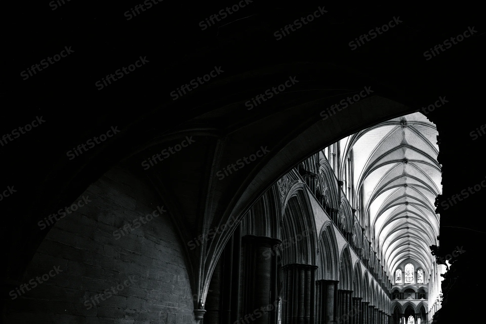 View through a dark archway into the illuminated nave of a gothic cathedral with vaulted ceiling and stone columns
