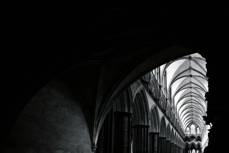 View through a dark archway into the illuminated nave of a gothic cathedral with vaulted ceiling and stone columns