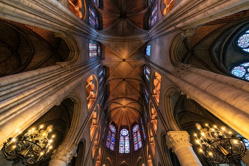 Upward view of a gothic cathedral interior with vaulted stone ceilings, stained glass windows, and ornate chandeliers