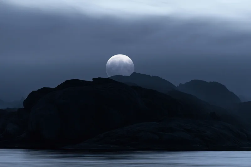 Full moon rising over rocky coast at night with fog and calm water