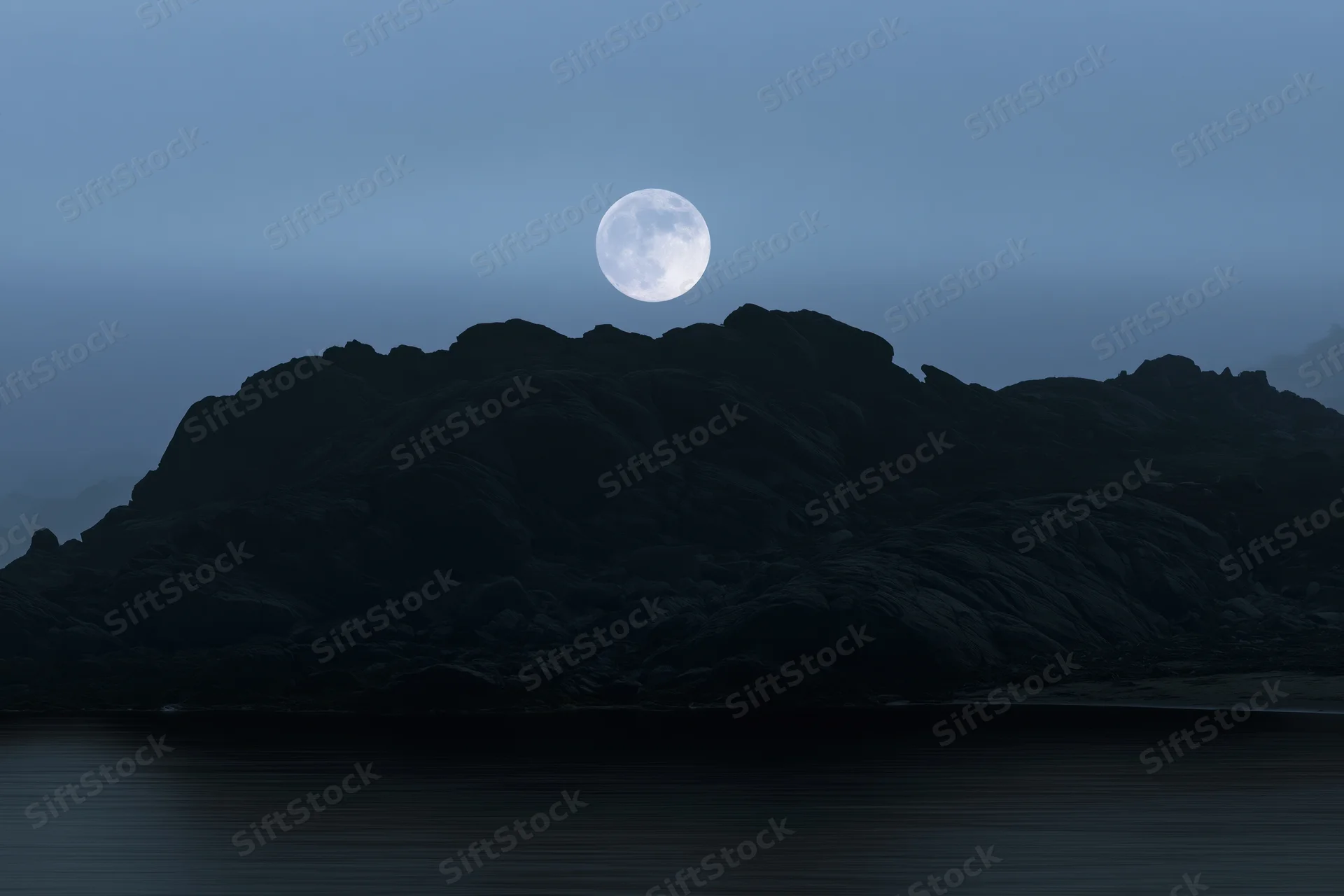 Full moon rising over rocky coastal silhouette at twilight