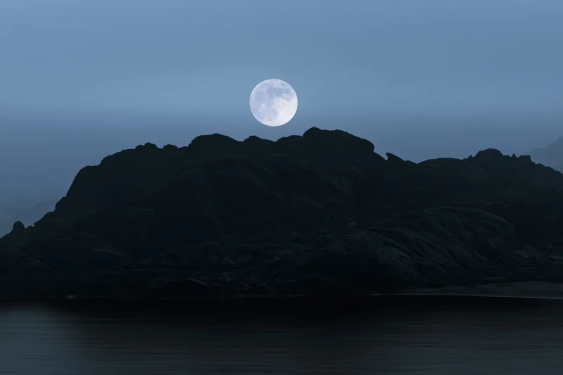 Full moon rising over rocky coastal silhouette at twilight