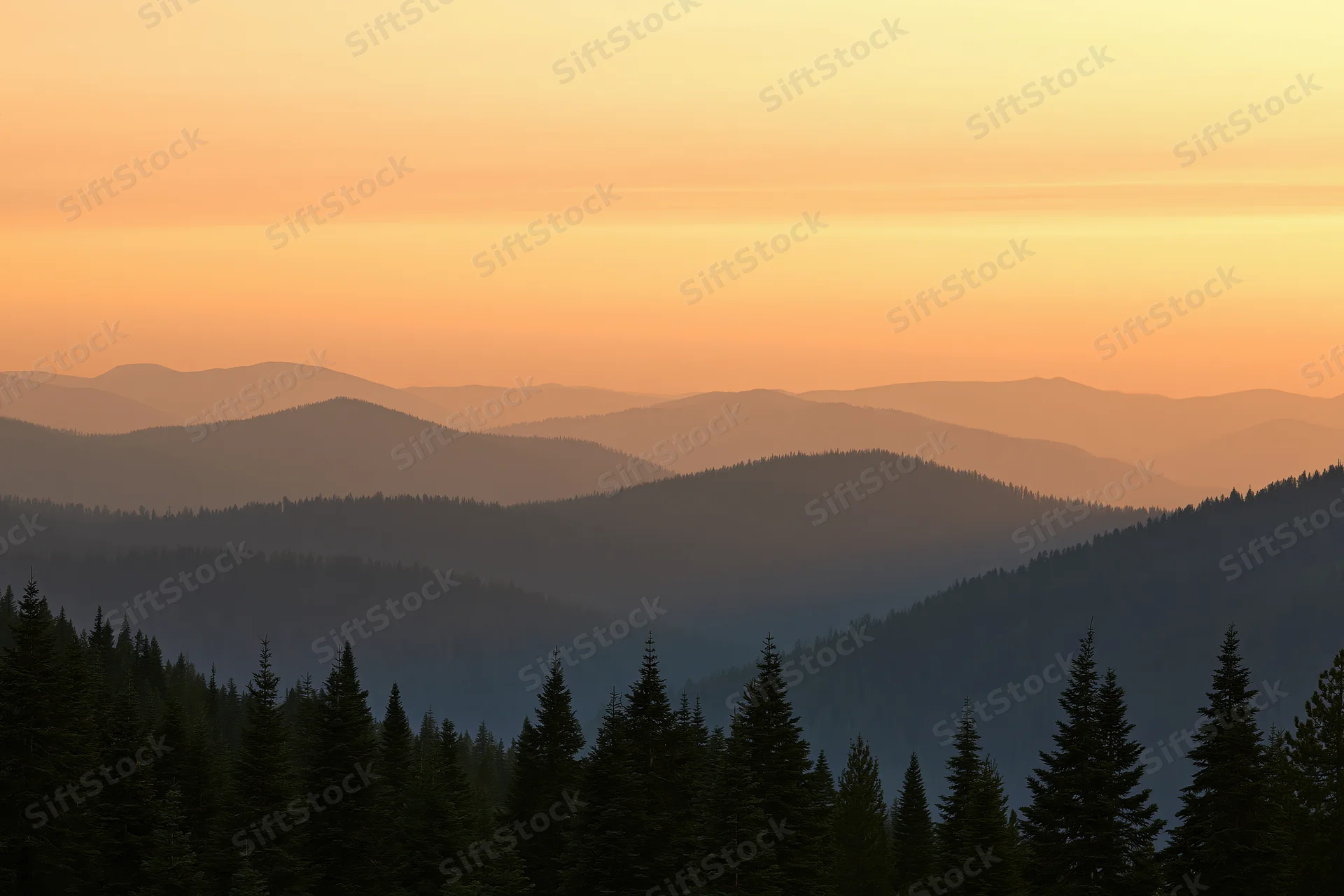 Layered mountain ridges receding into hazy distance with evergreen forest in foreground at sunset