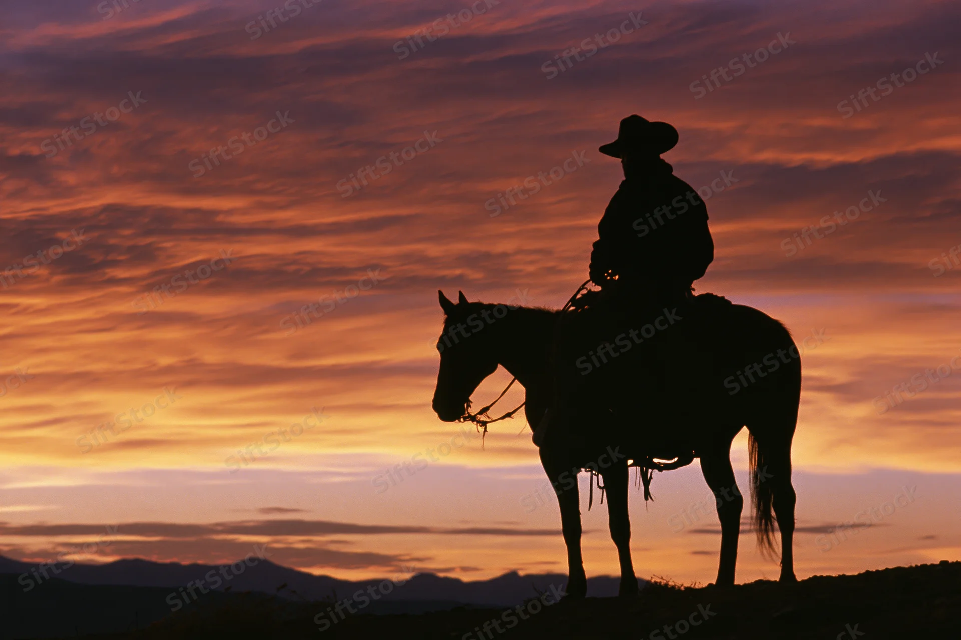 Cowboy riding horse in silhouette against sunset sky with mountains in distance