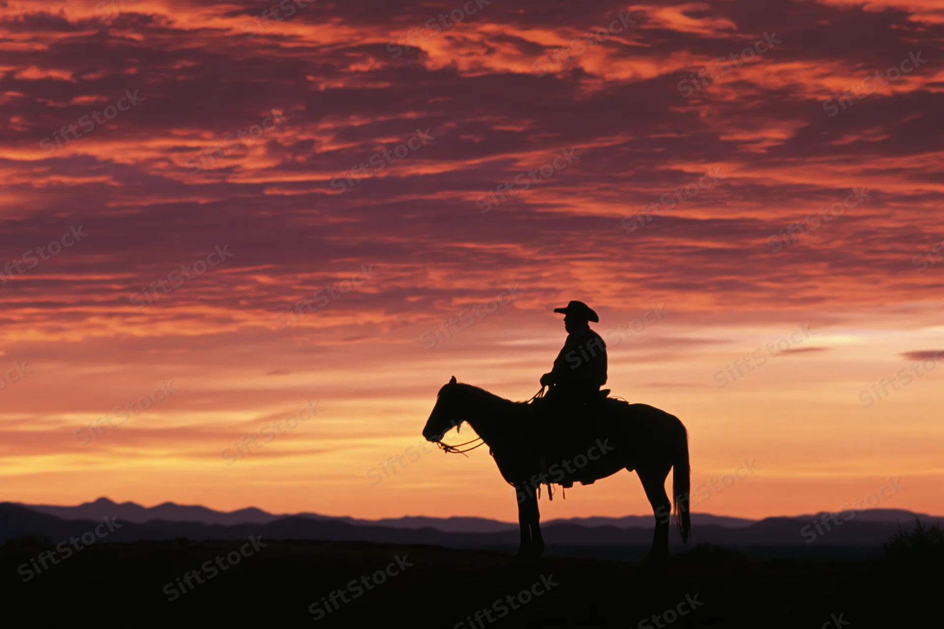 Cowboy riding horse in silhouette against sunset sky with distant mountains