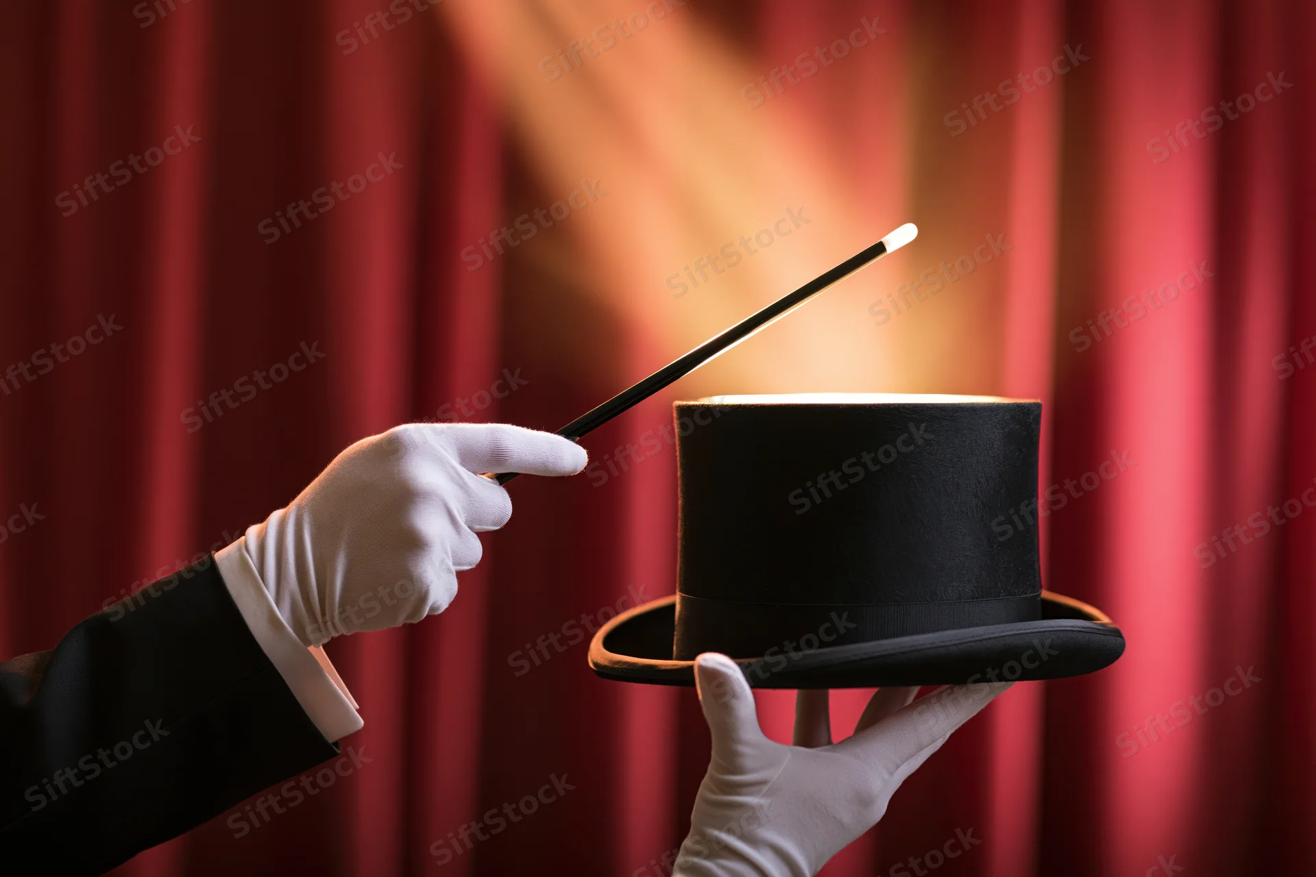 Magician's gloved hands holding a black top hat and pointing a wand against a red curtain backdrop