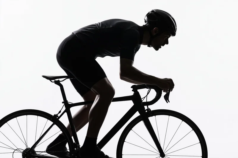 Male cyclist in aerodynamic forward-leaning posture riding a road bicycle against white background