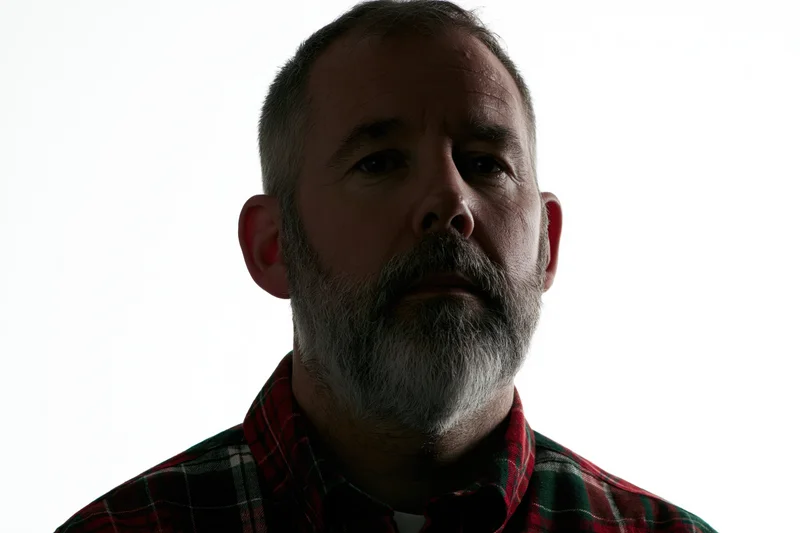 Middle-aged man with short grey beard and plaid shirt in studio portrait against white background