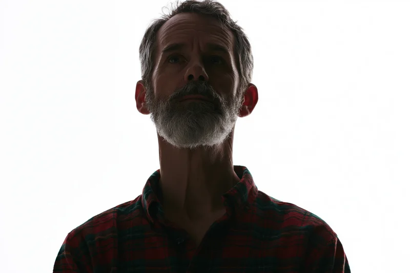 Middle-aged man with grey beard and plaid shirt in silhouette against white background
