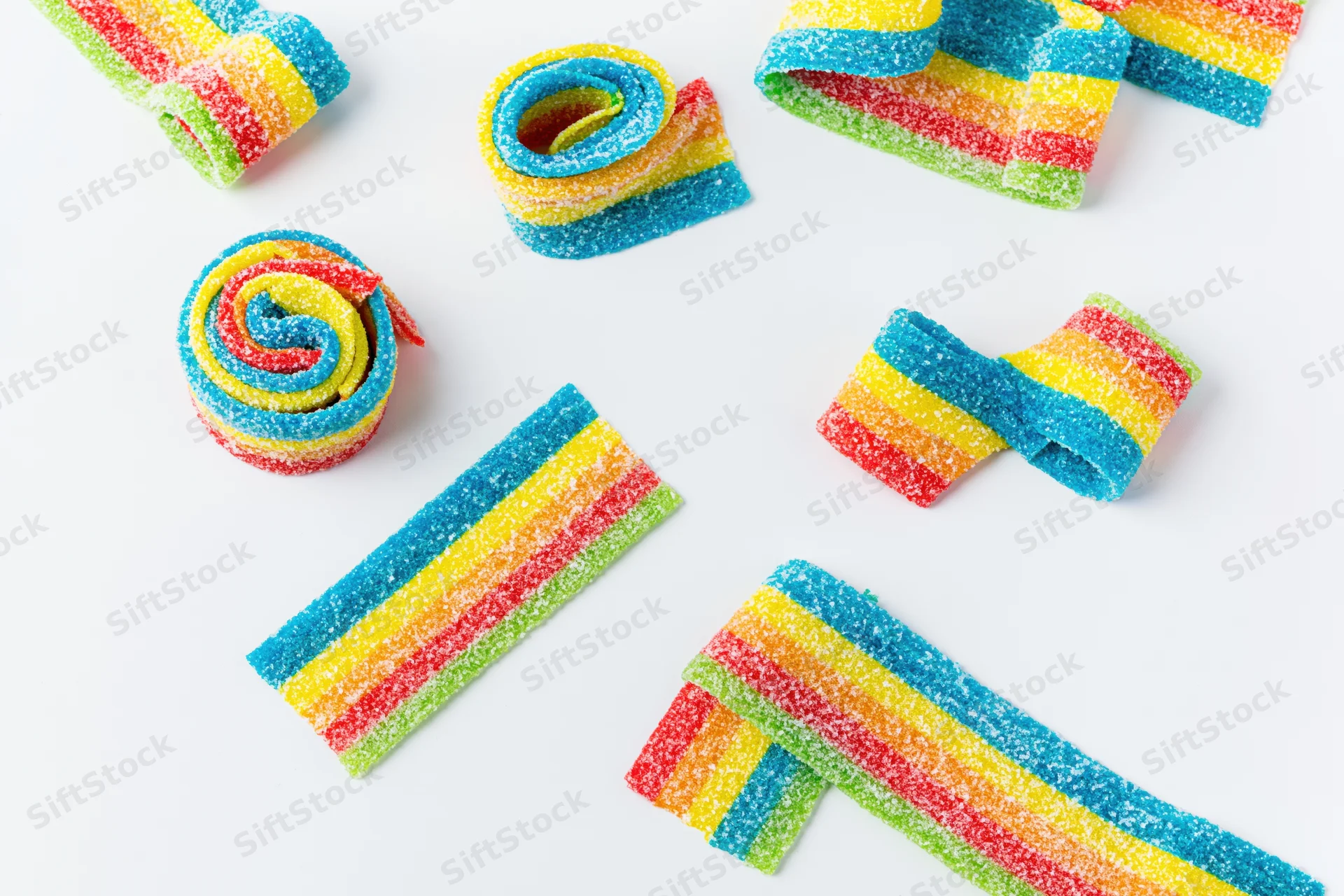 Sour rainbow gummy candy belts arranged in various shapes on white background