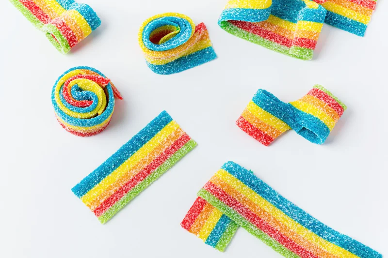 Sour rainbow gummy candy belts arranged in various shapes on white background