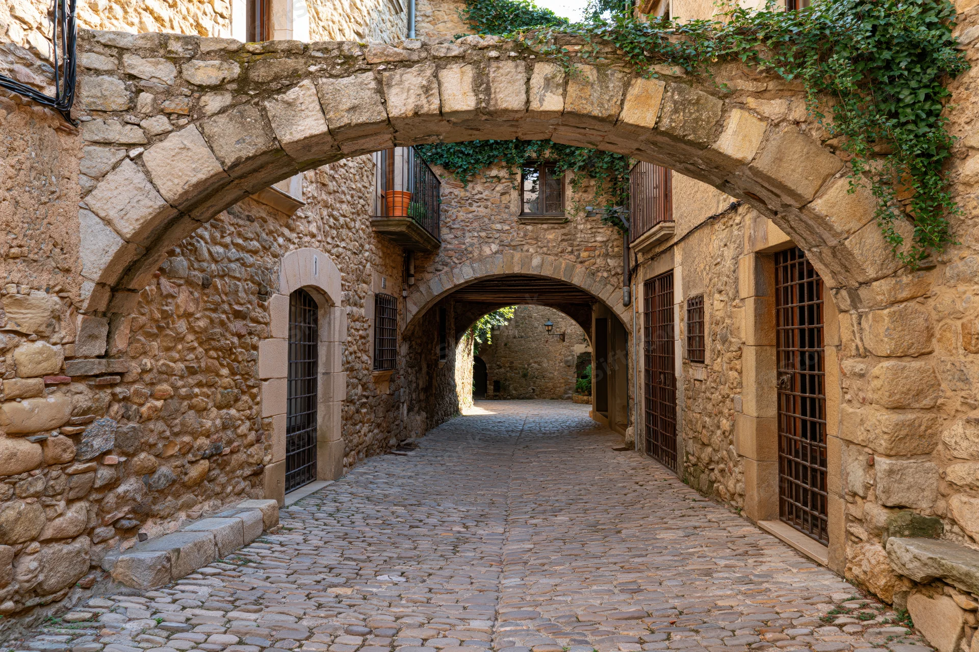 Narrow cobblestone alley under stone arches in a medieval catalan village