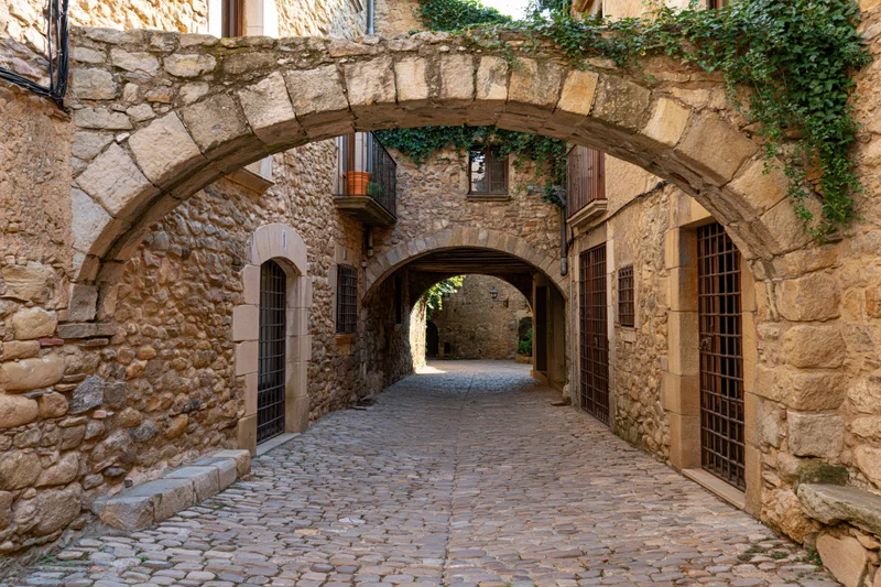 Narrow cobblestone alley under stone arches in a medieval catalan village