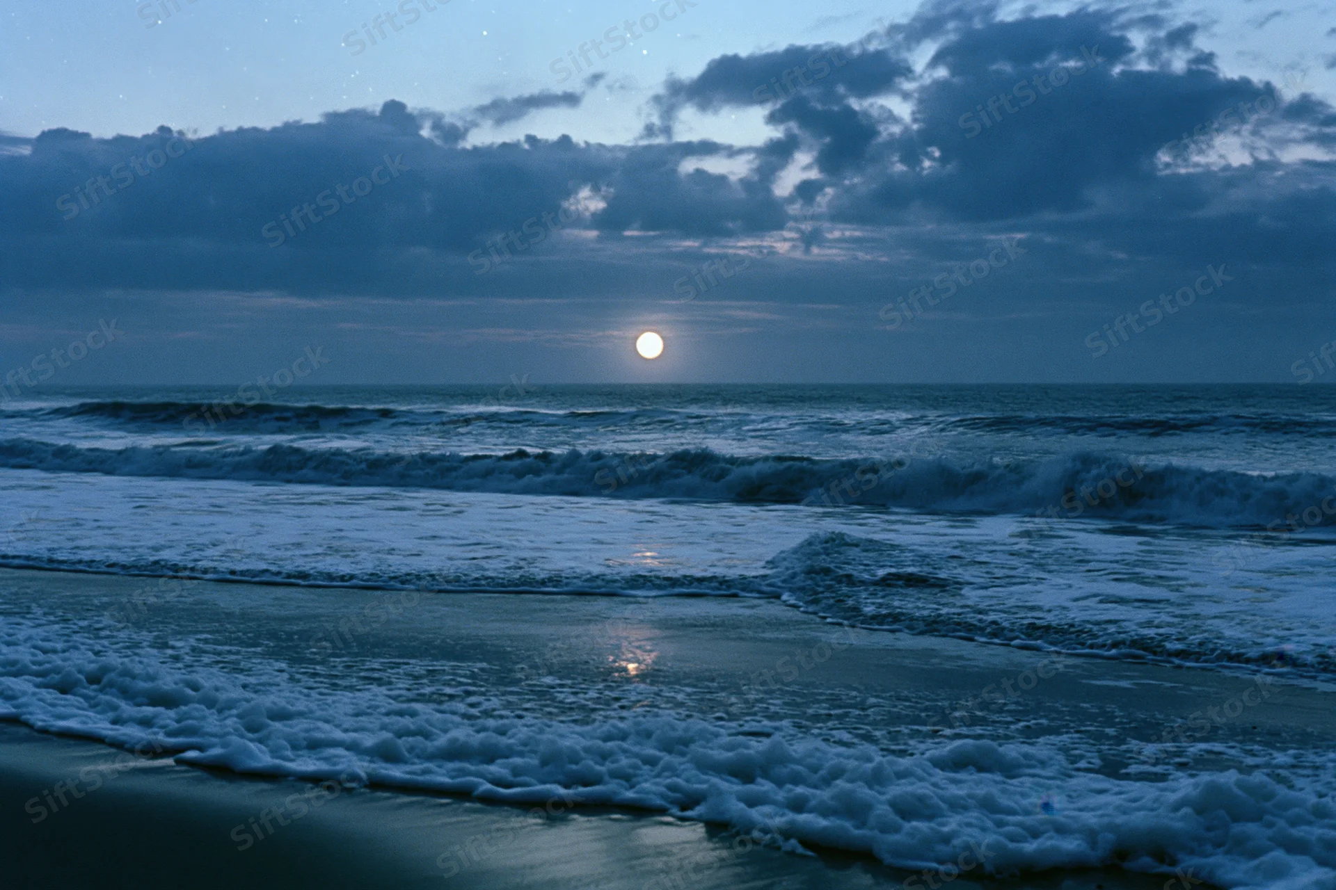 Ocean waves breaking on a wet sandy beach at night under moonlight