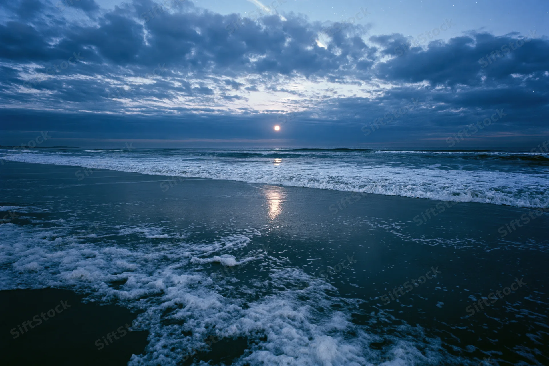 Ocean waves breaking on a wet sandy beach at night under moonlight