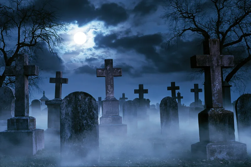 Old cemetery at night with weathered stone crosses and tombstones in fog under a full moon