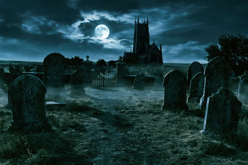 Old graveyard at night with crumbling headstones lining a path toward a gothic church under a full moon