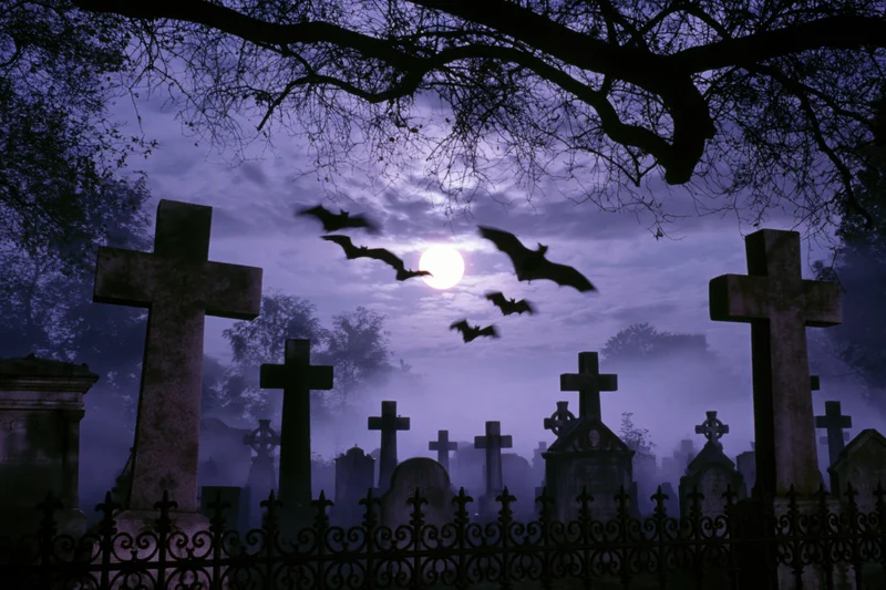 Old graveyard at night with stone cross headstones and flying bats under a full moon, surrounded by fog and bare trees