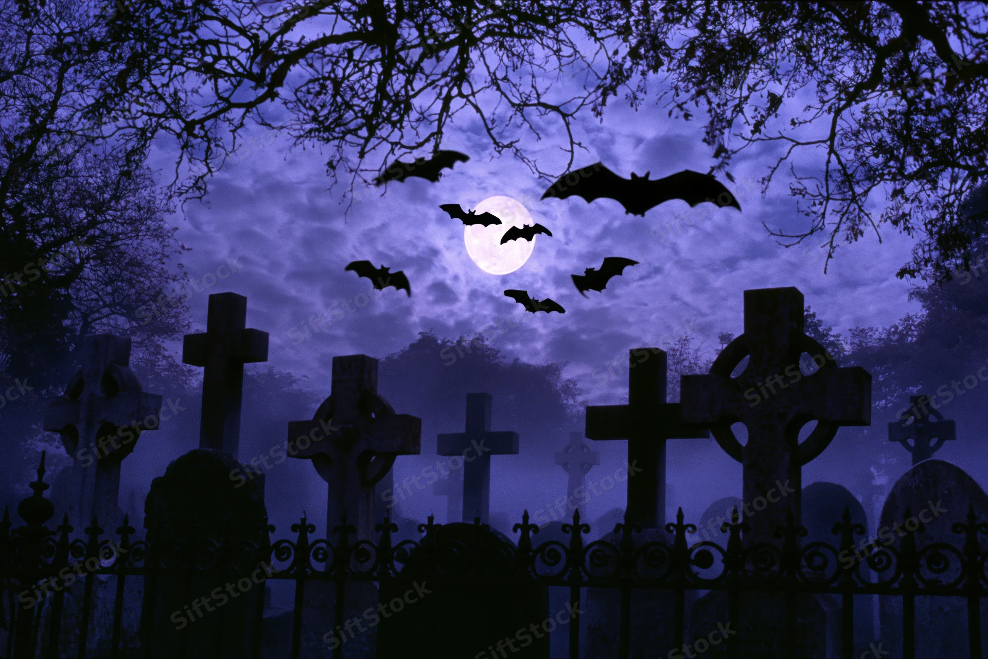 Silhouetted bats flying over old stone crosses in a foggy graveyard at night under a full moon