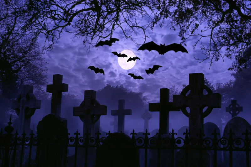 Silhouetted bats flying over old stone crosses in a foggy graveyard at night under a full moon