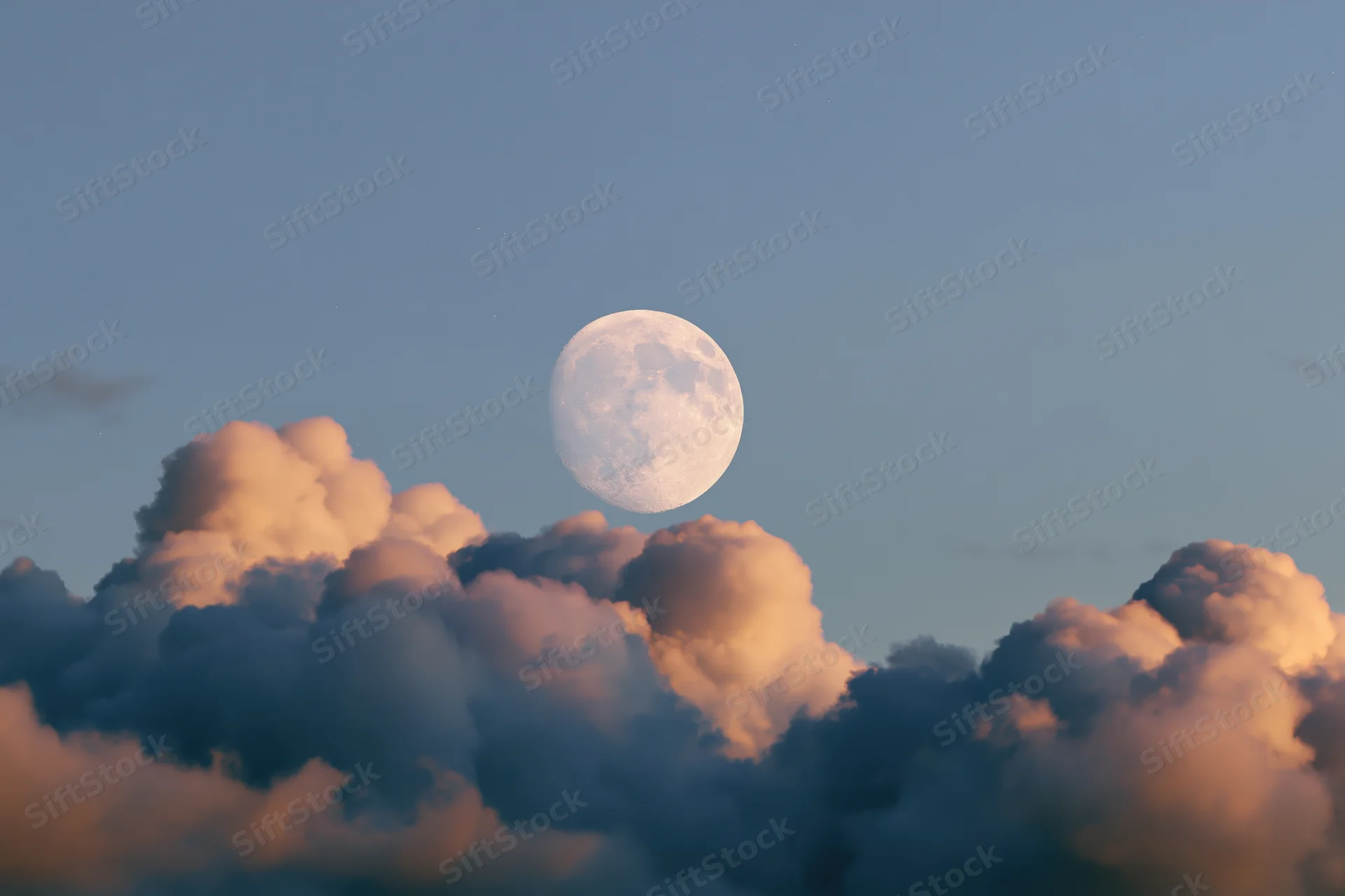Full moon rising above a bank of cumulus clouds at twilight