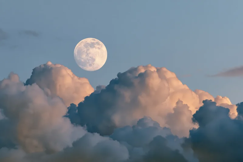Full moon rising above a bank of cumulus clouds at twilight