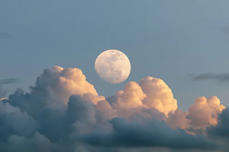 Full moon rising above a bank of dramatic cumulus clouds at twilight