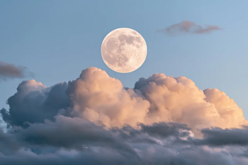 Full moon rising above a bank of cumulus clouds at twilight