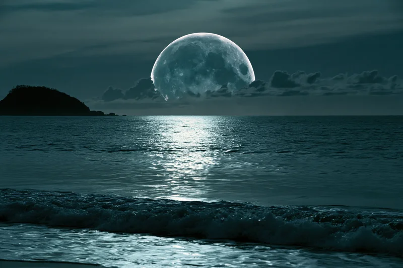 Oversized full moon rising over calm ocean at night with moonlight reflecting on water surface