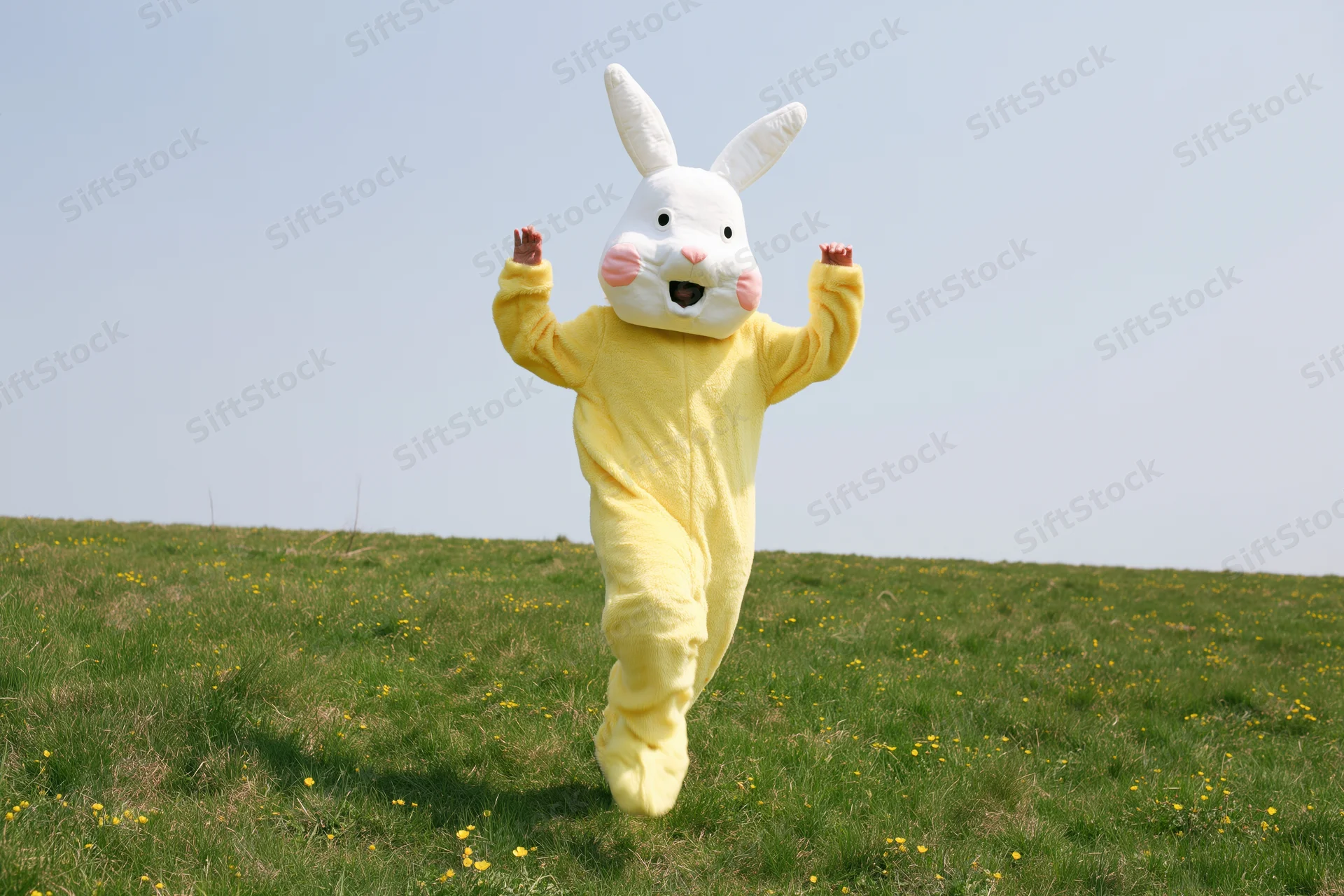 Person in yellow easter bunny costume running across grassy field