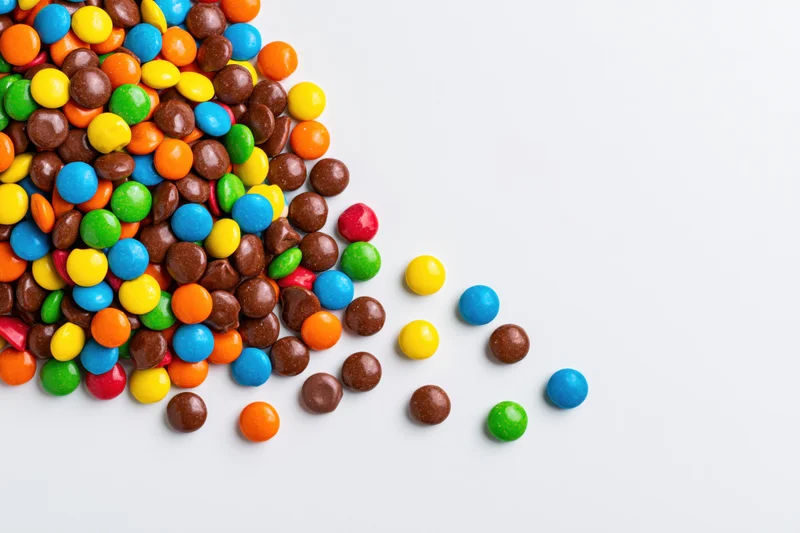 Pile of colorful button candies scattered across white background with copyspace