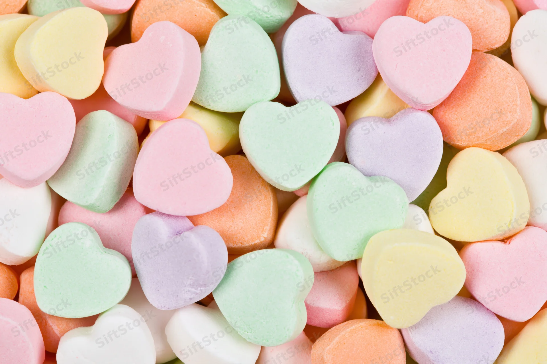 Pastel heart-shaped candies piled together filling the frame