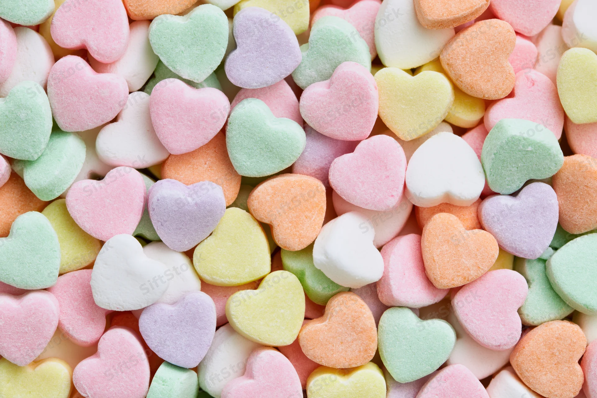 Pastel heart-shaped candy piled together filling the frame