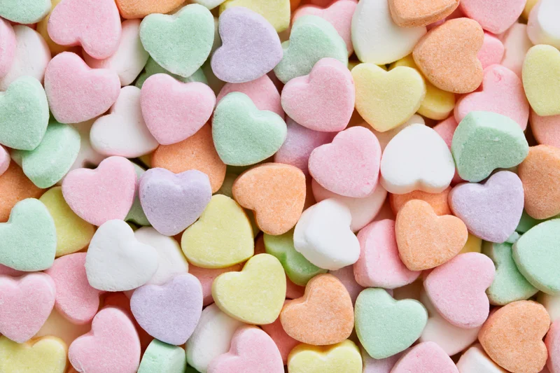 Pastel heart-shaped candy piled together filling the frame