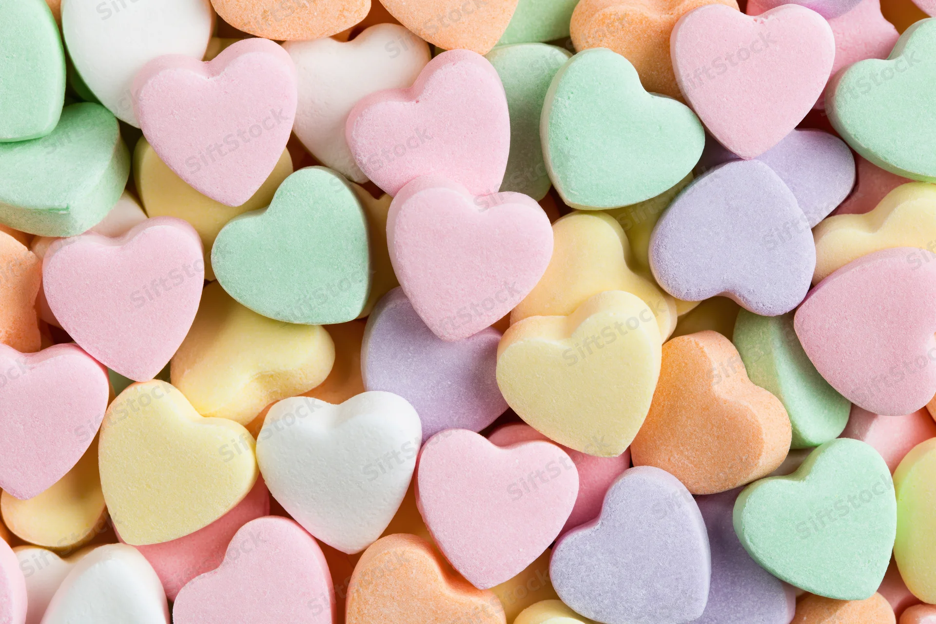 Pastel heart-shaped candies piled together in a close-up flat lay view