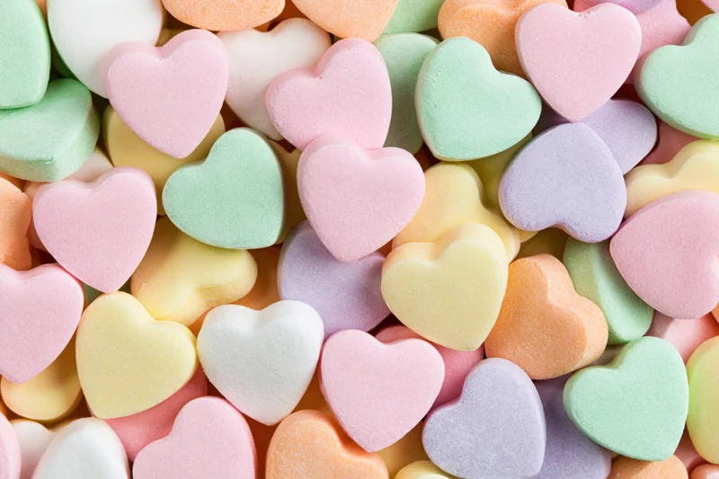 Pastel heart-shaped candies piled together in a close-up flat lay view
