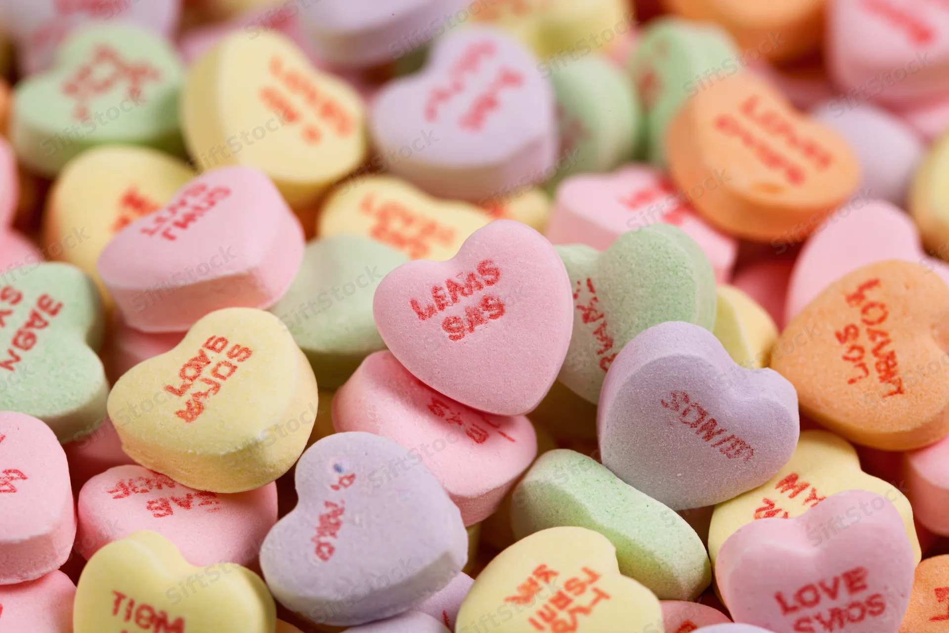 Pile of pastel heart-shaped candies with love messages scattered across frame