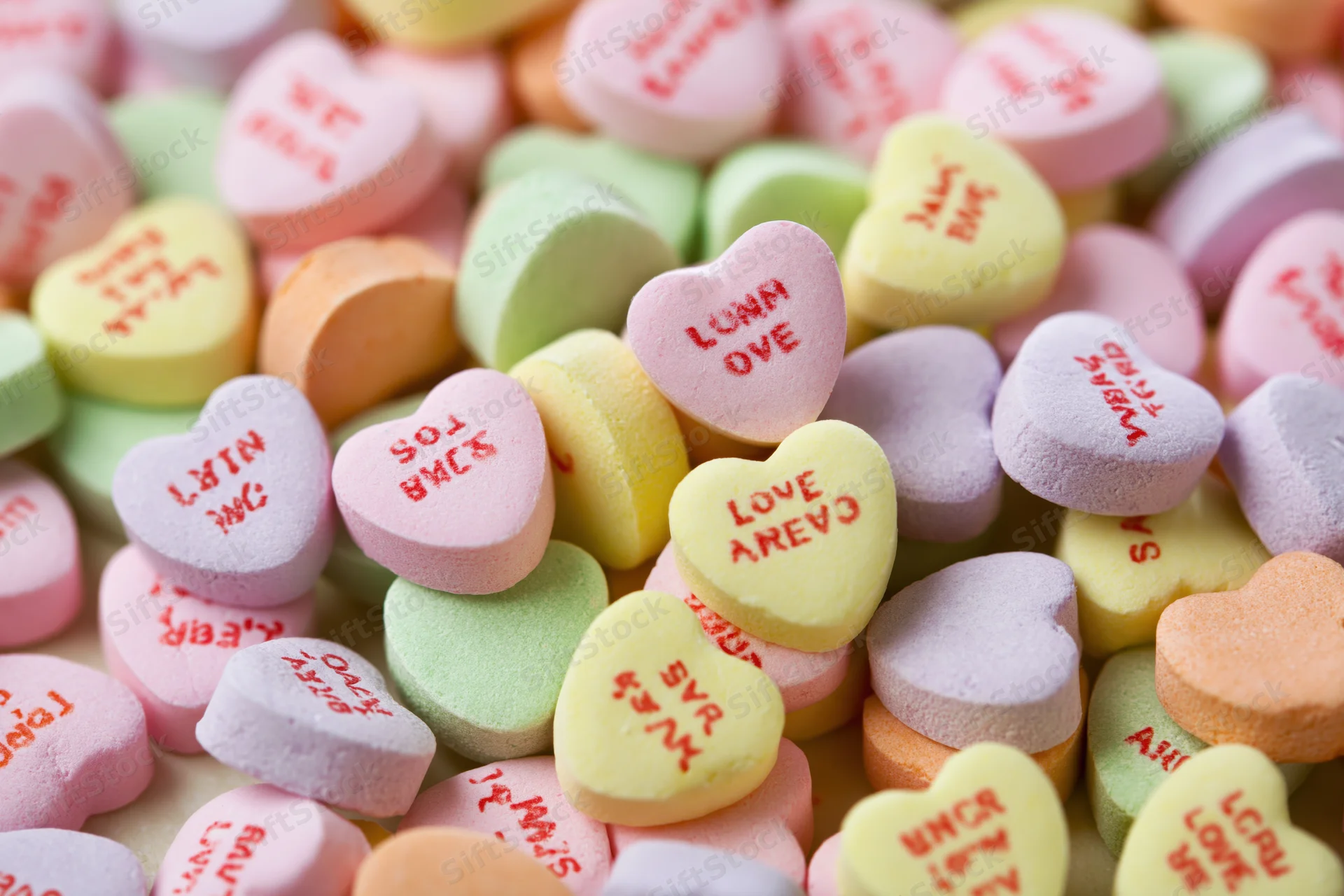 Pile of pastel heart-shaped candies with love messages filling the frame