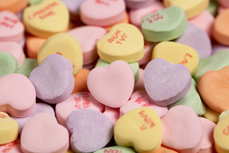 Pile of pastel heart-shaped candies with printed messages filling the frame