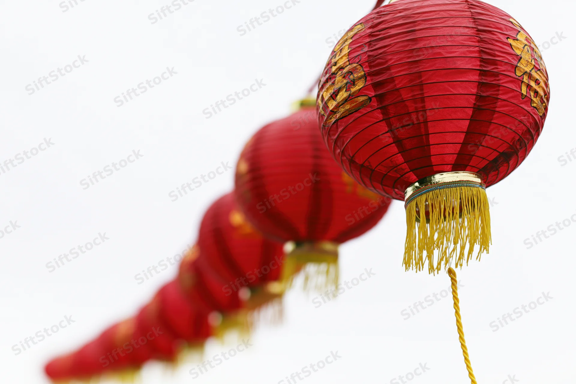Row of red paper lanterns with golden tassels and calligraphy hanging on a string against white background