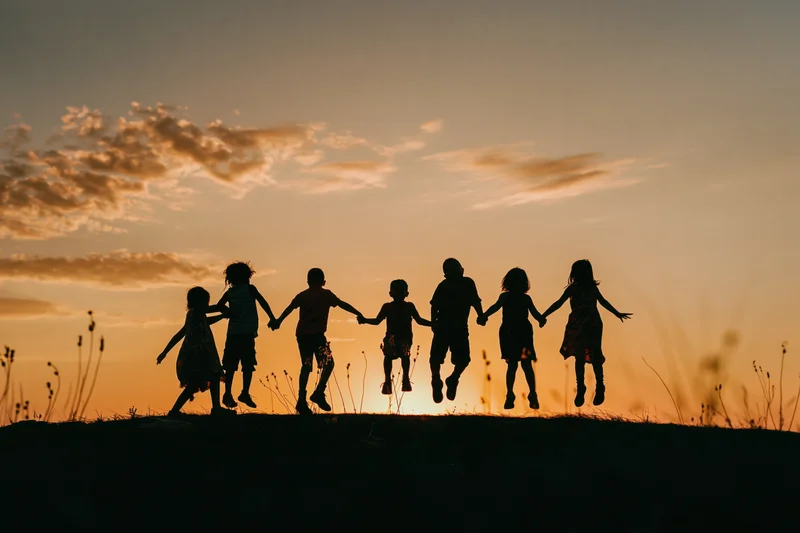 Silhouetted children holding hands and jumping on a hill at sunset