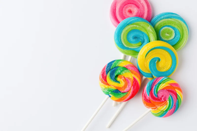 Colorful swirl lollipops on white sticks arranged on a plain white surface with copyspace