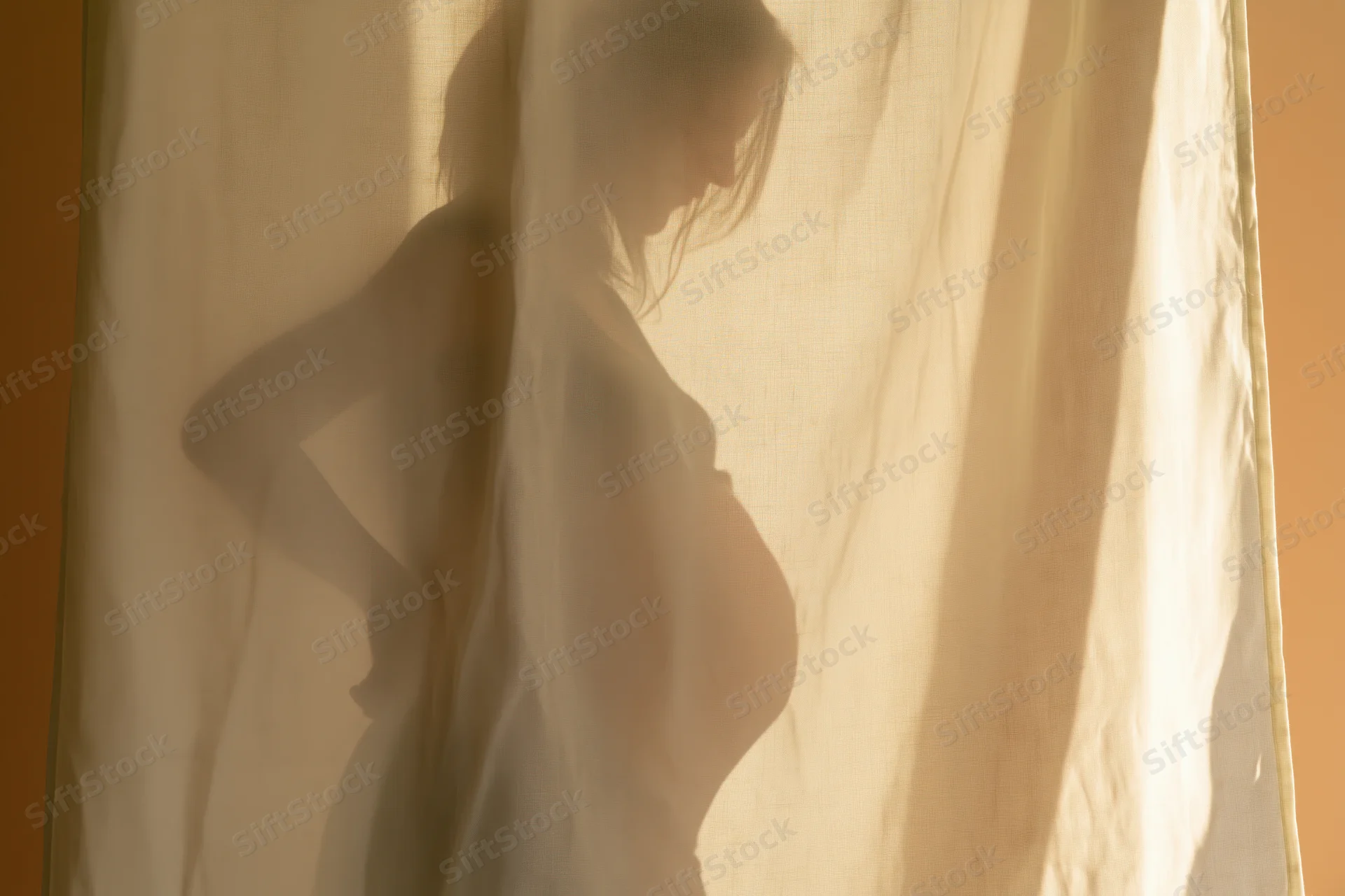 Pregnant woman's silhouette cast on sheer linen curtain, side profile with hand on hip, soft warm light indoors