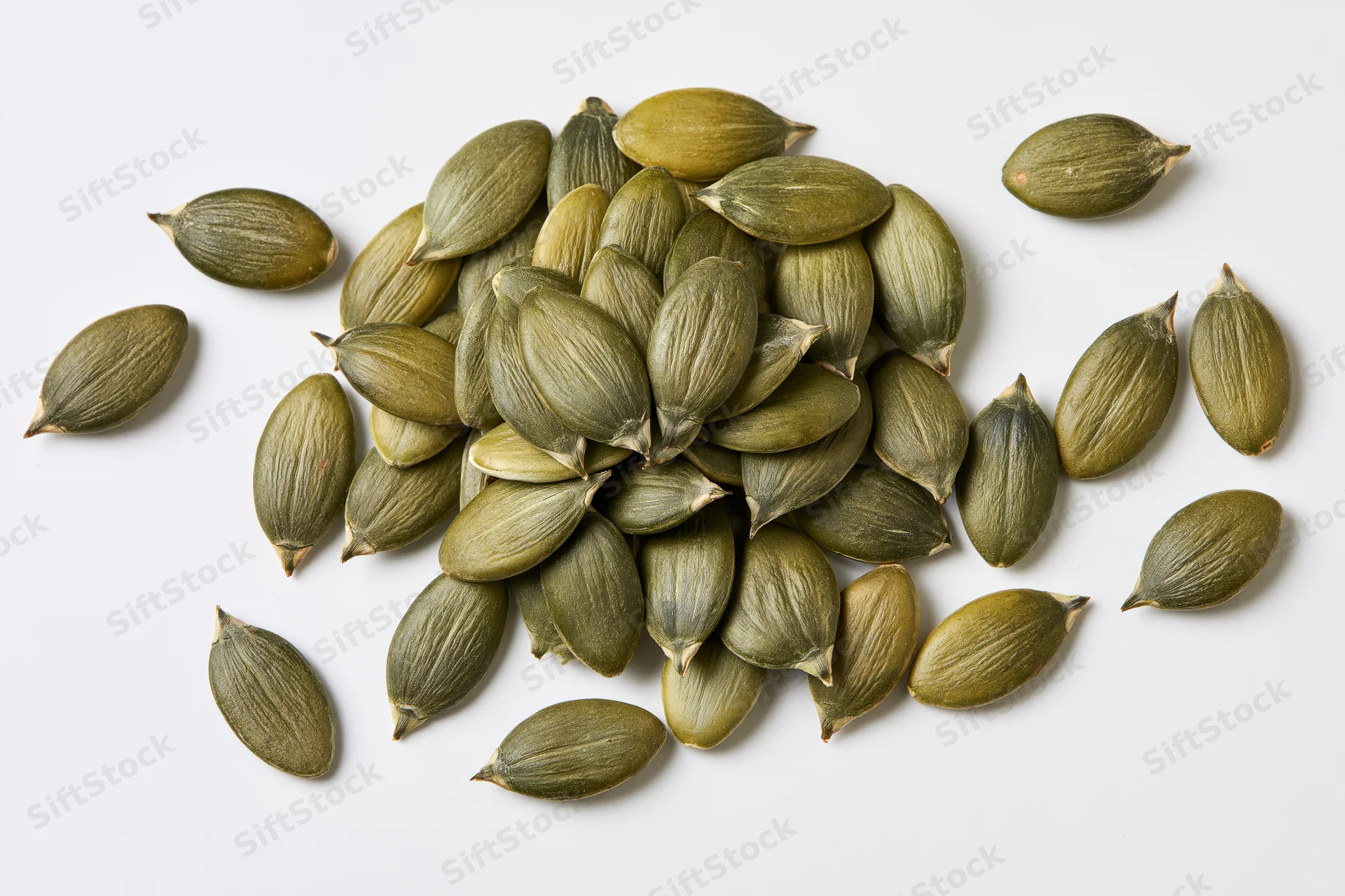 Shelled pumpkin seeds scattered loosely on a white surface