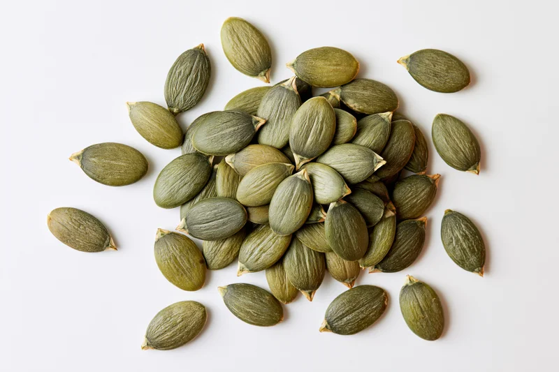 Shelled pumpkin seeds scattered loosely on a white surface