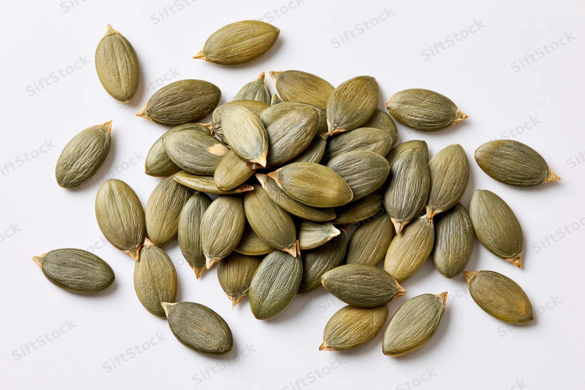 Shelled pumpkin seeds scattered loosely on a white surface