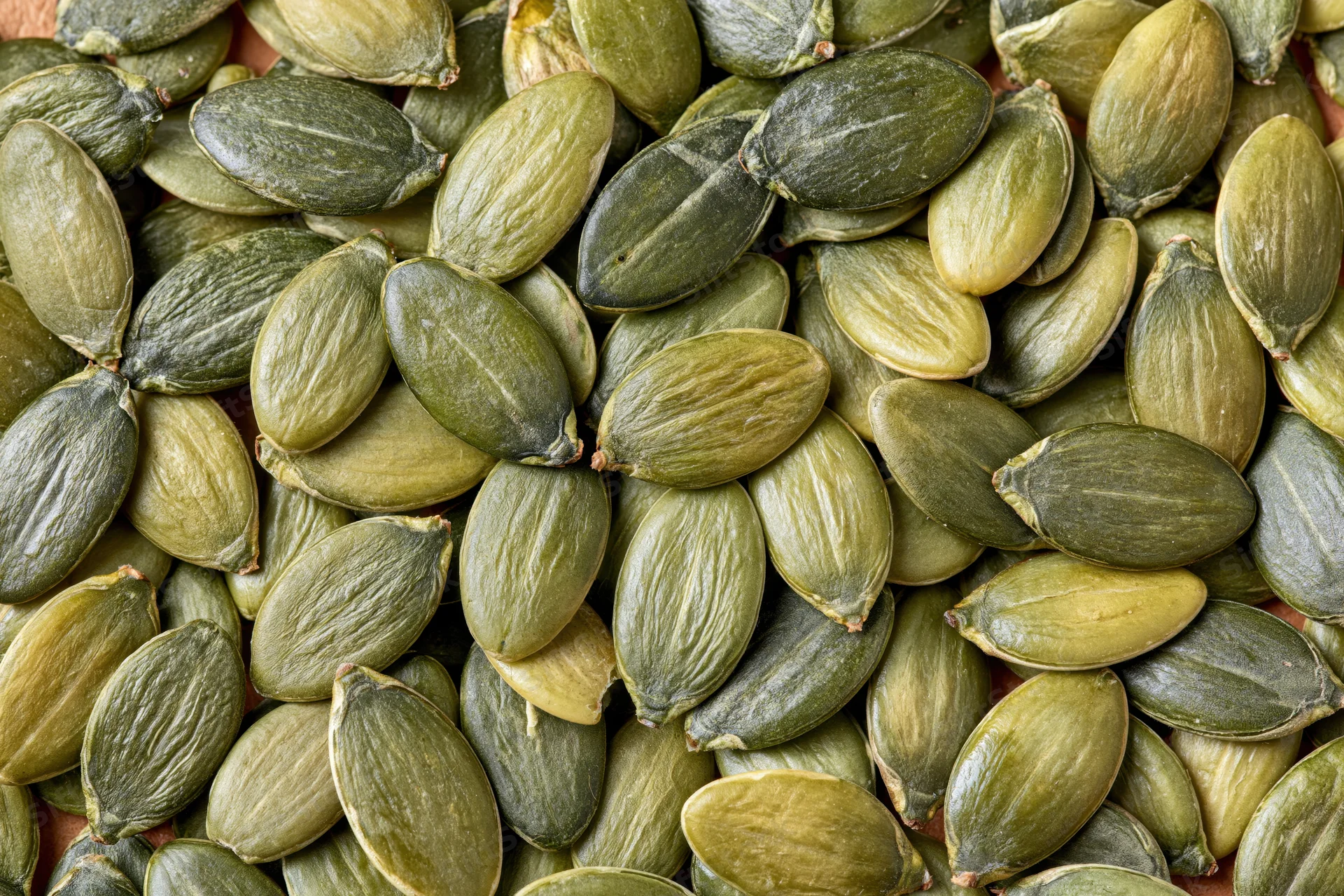 Shelled pumpkin seeds scattered across a flat surface filling the frame