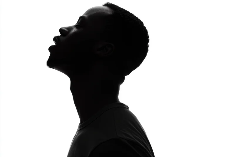 Silhouette of a young man in profile looking upward against white background